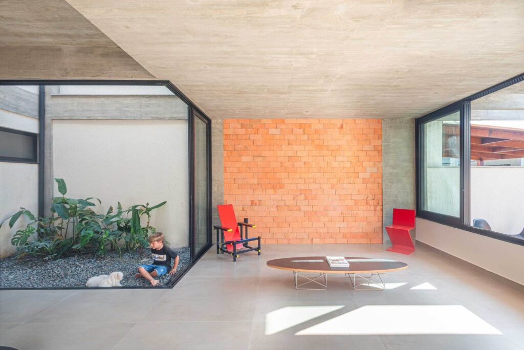 Modern interior lounge area next to a glass-enclosed internal garden with a textured brick wall.