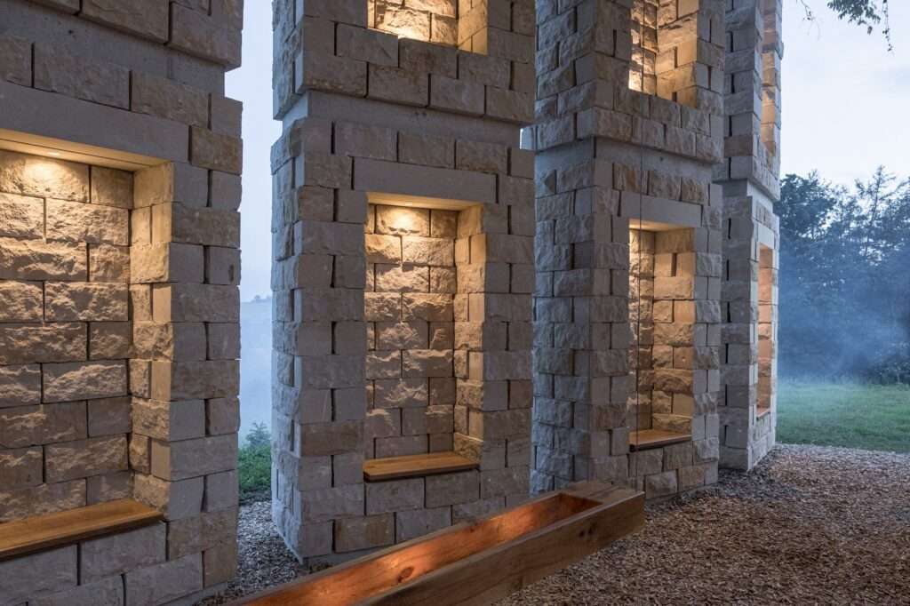 Night view of the Open Chapel with warm interior lighting illuminating the sandstone niches and wooden benches.