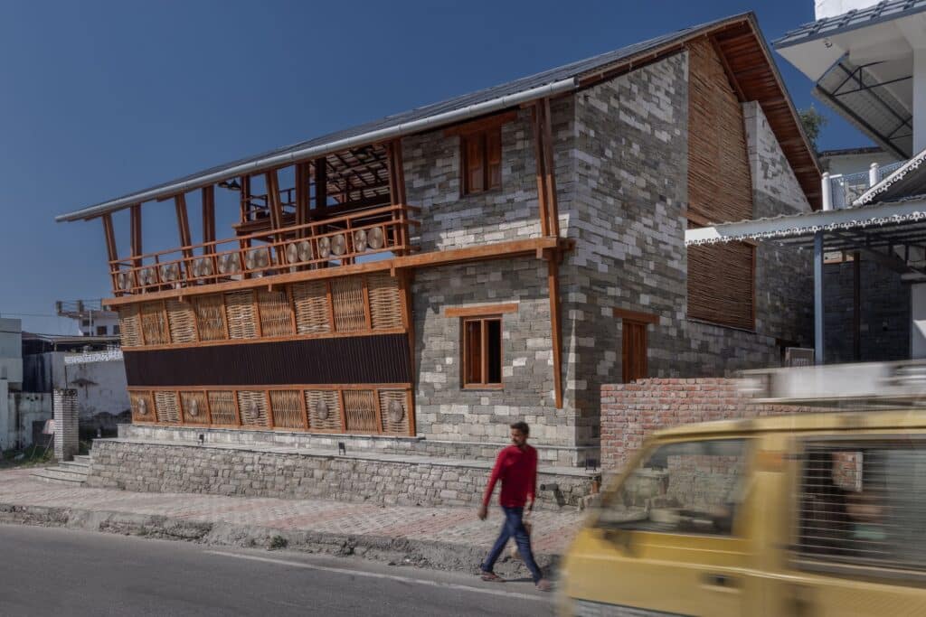 Street-side view of the project showing the stone-clad building integrated into the urban fabric with a passing vehicle in the foreground.