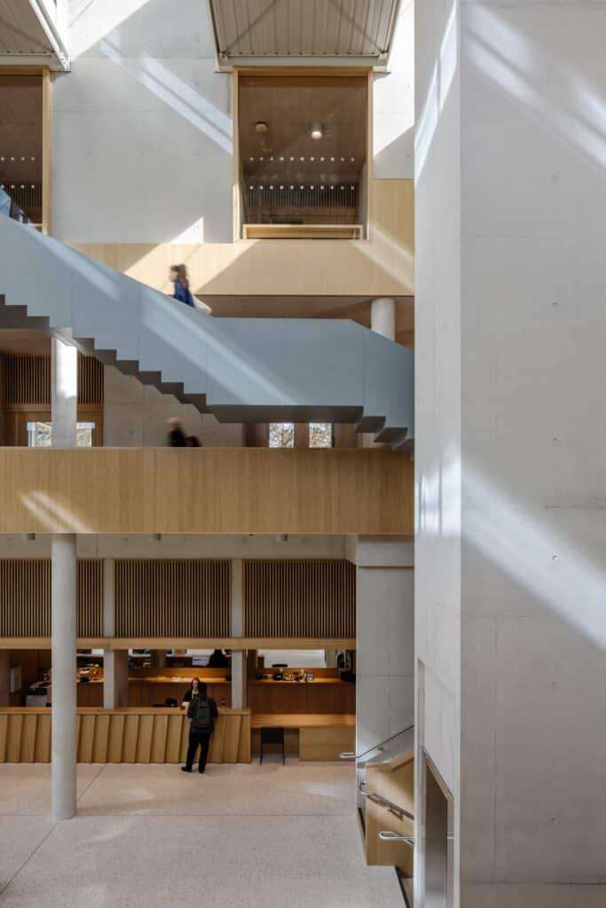 Internal view of the student centre showing the reception desk, multiple floor levels, and a minimalist grey staircase.