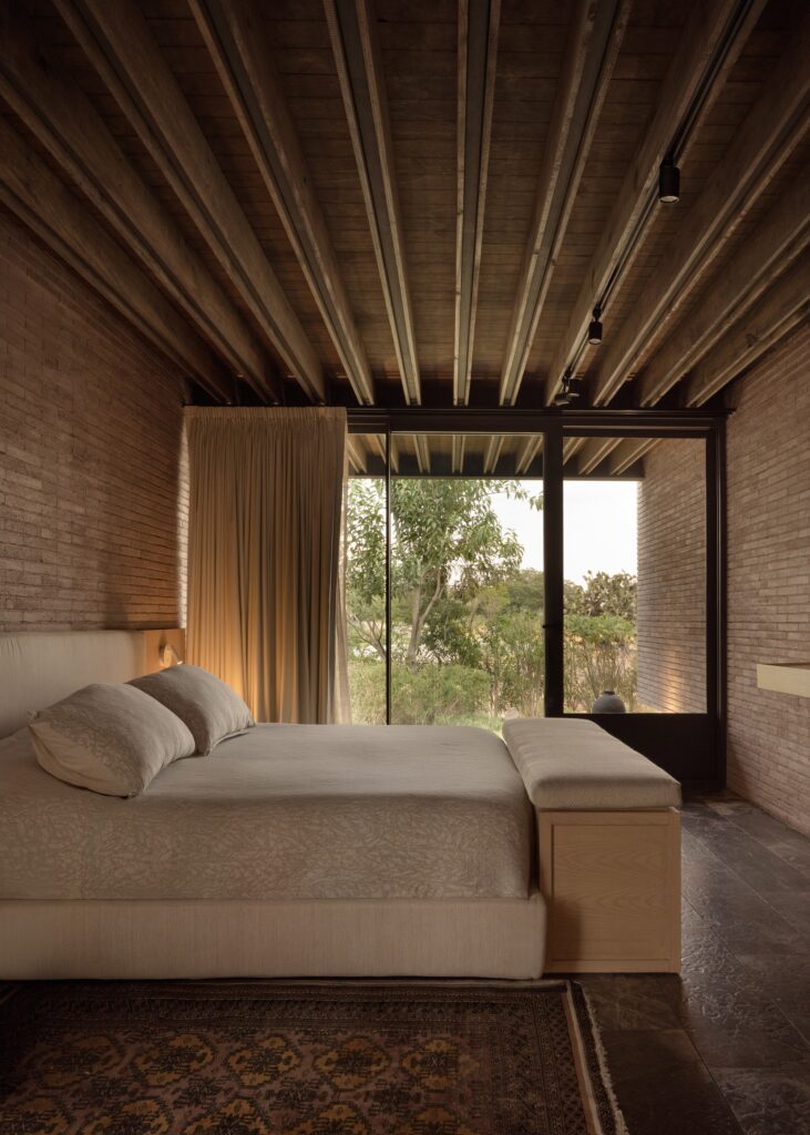 Minimalist master bedroom in Capuchinas House with exposed concrete walls and wooden ceiling beams overlooking the garden.