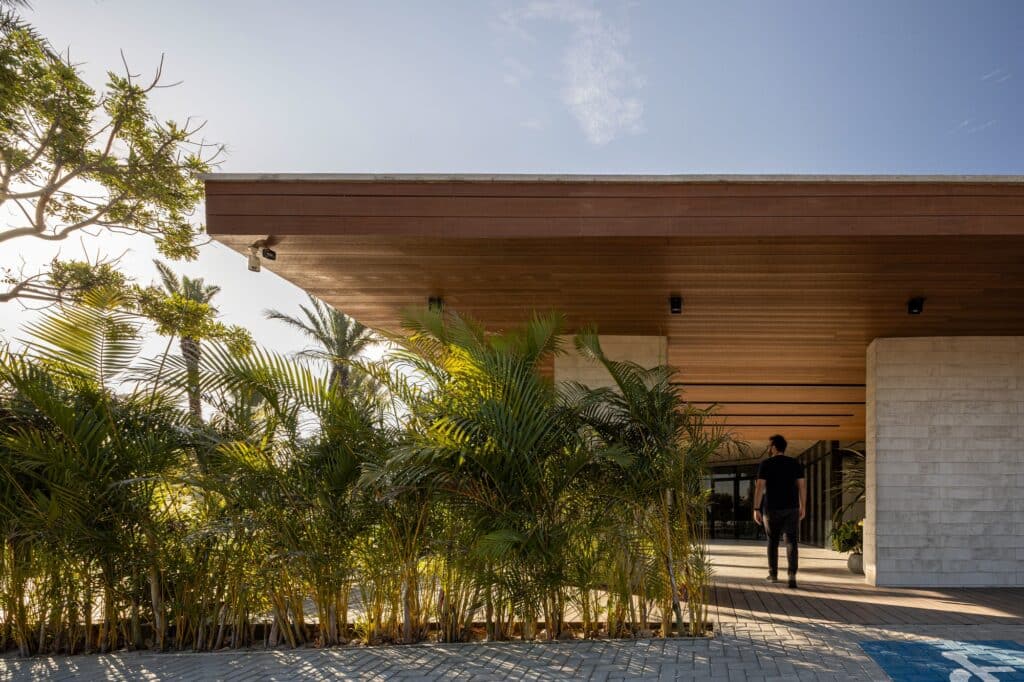 Pedestrian entrance path surrounded by tropical greenery leading into the open-plan architectural structure.