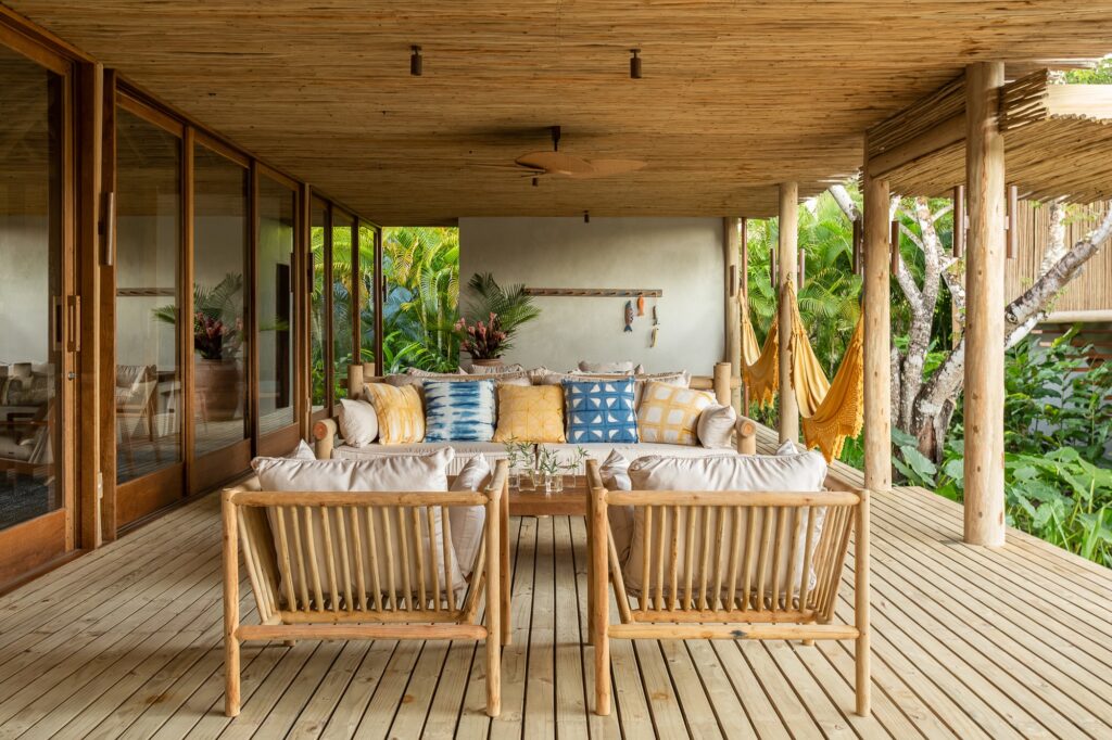 Cozy outdoor lounge area with wooden armchairs, patterned pillows, and yellow hammocks under a timber ceiling.