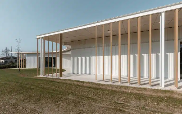 View from the perimeter porch showing the rhythmic shadows cast by wooden louvers on the white corrugated wall.