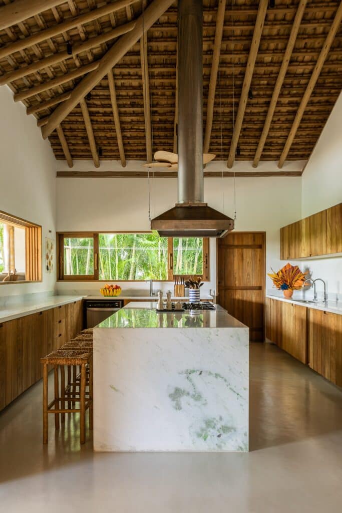 Modern interior kitchen with a large marble island, high wooden ceilings, and expansive windows overlooking the garden.
