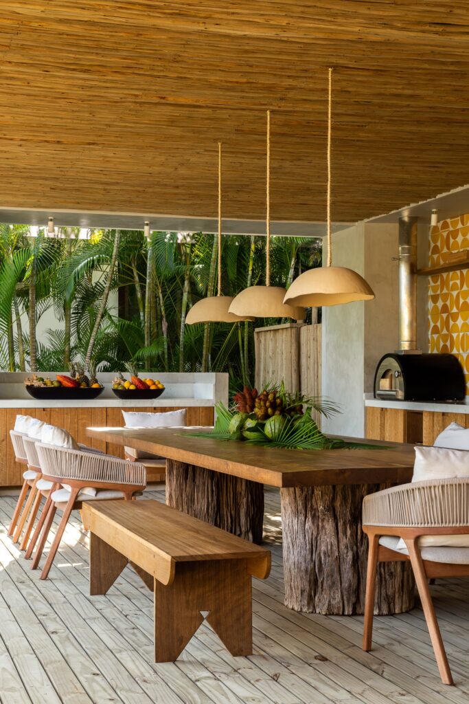 Detailed view of a rustic wooden dining table with heavy trunk-like legs and pendant clay lamps.