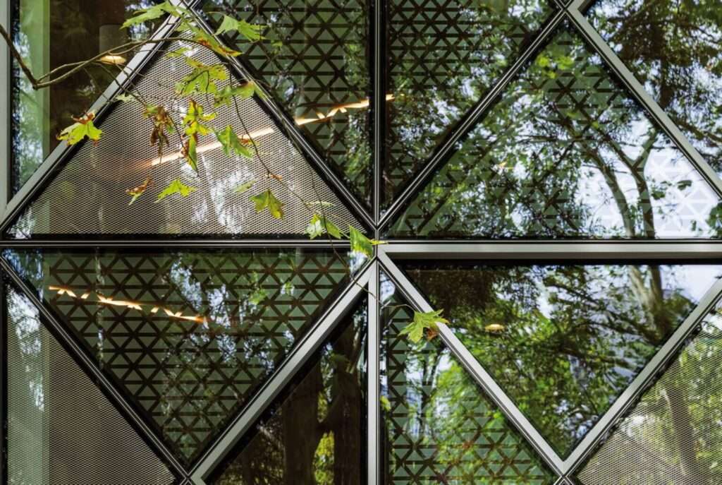 Close-up of triangular glass panels arranged into a square, showing mesh patterns and reflected tree branches.