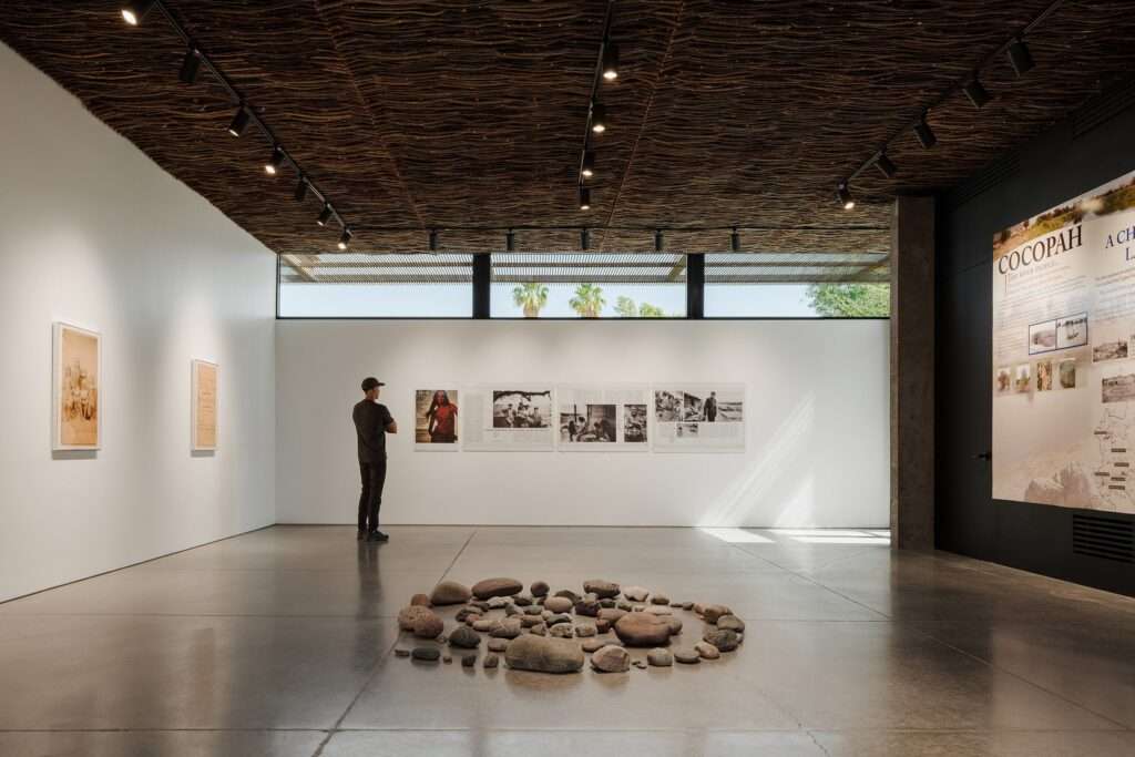 Interior of Cocopah Museum gallery with woven willow ceiling, a visitor viewing wall exhibits and a stone circle on the floor