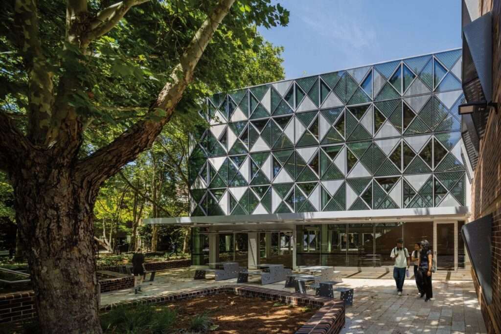 An outdoor courtyard with metal seating benches next to a glazed building facade under a canopy.