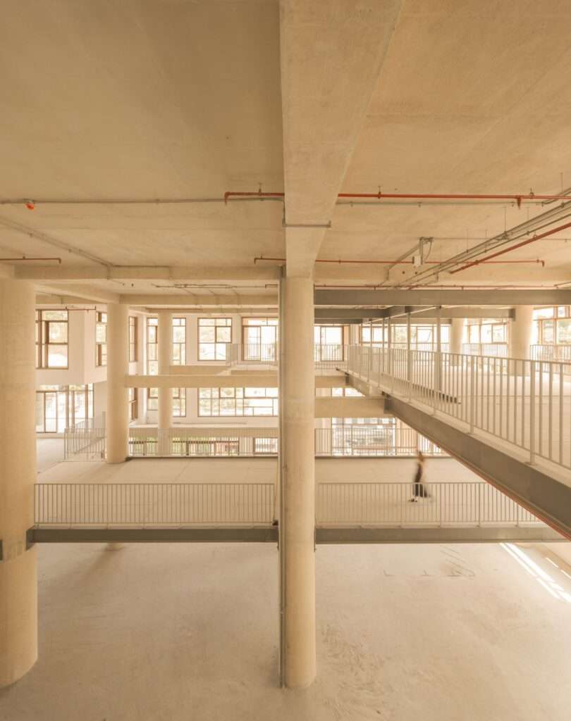 Unfinished interior space with exposed concrete columns, high ceilings, steel walkways, and large windows.