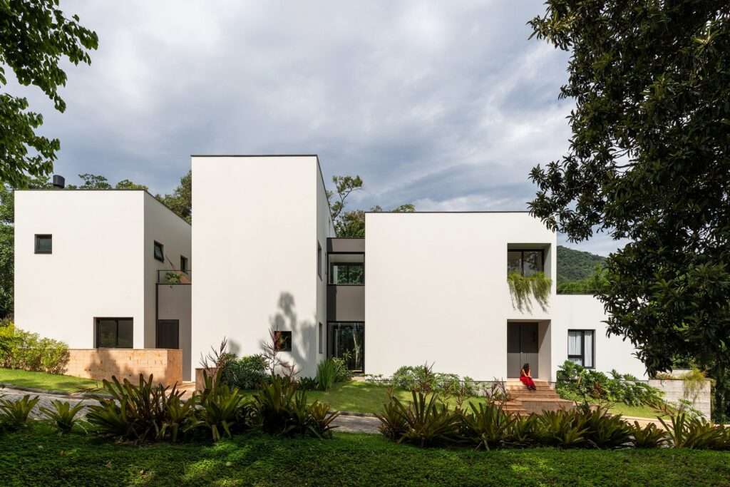 Minimalist white cubic volumes of Bina House in Florianópolis surrounded by lush Atlantic Forest landscaping.