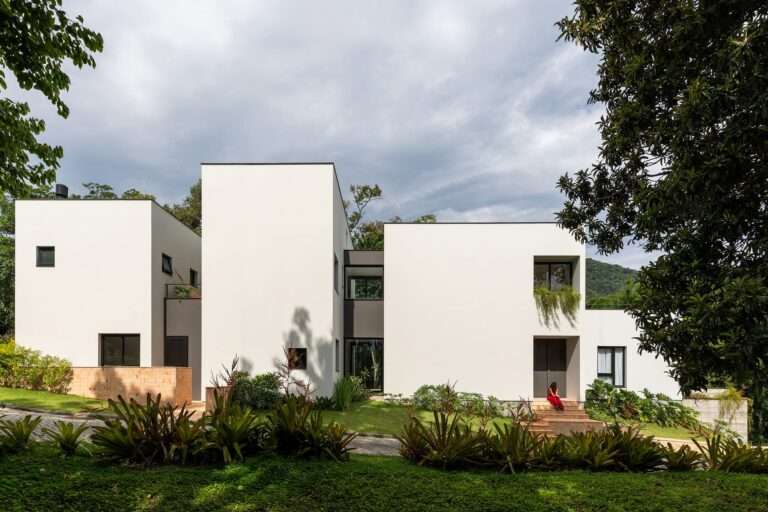 Minimalist white cubic volumes of Bina House in Florianópolis surrounded by lush Atlantic Forest landscaping.