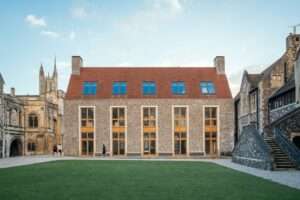 Exterior facade of the Rausing Science Centre at The King's School featuring flint walling, limestone trim, large vertical windows, and a red tiled roof facing a green courtyard.