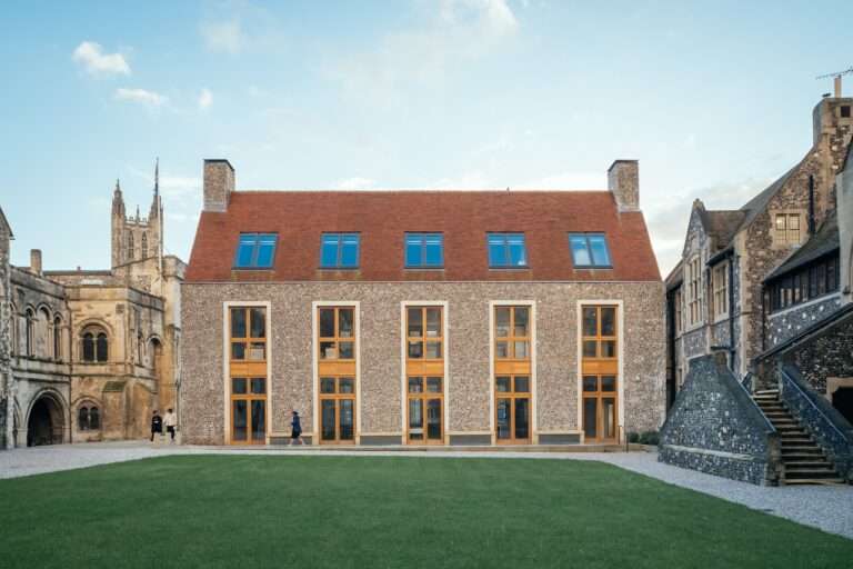 Exterior facade of the Rausing Science Centre at The King's School featuring flint walling, limestone trim, large vertical windows, and a red tiled roof facing a green courtyard.