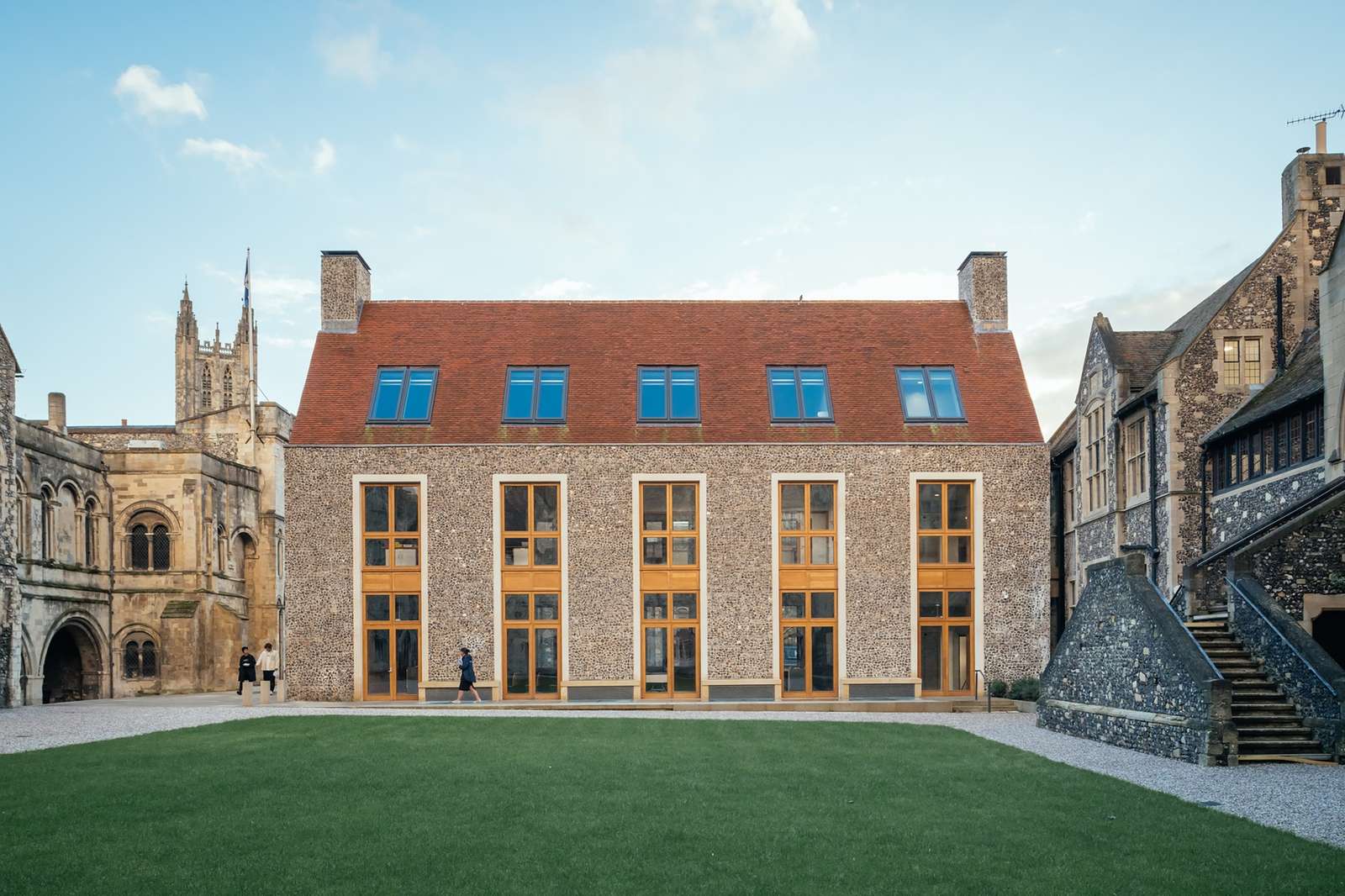 Exterior facade of the Rausing Science Centre at The King's School featuring flint walling, limestone trim, large vertical windows, and a red tiled roof facing a green courtyard.