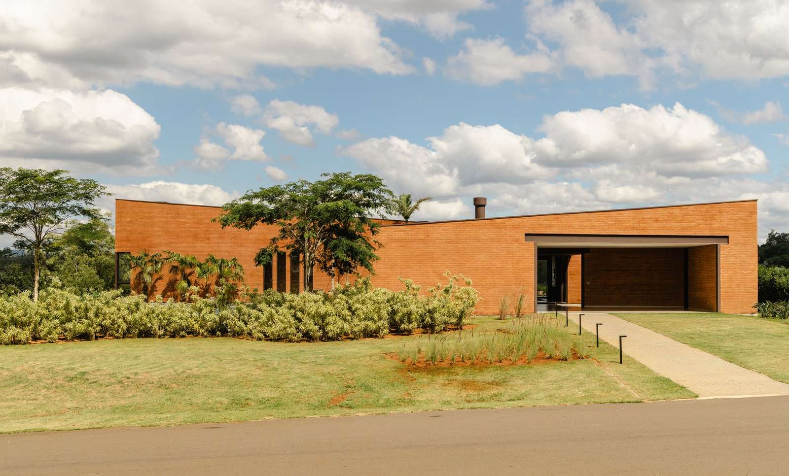 Exterior view of Casa Plateau featuring two parallel volumes made of earth-cement bricks on a sloped landscape.