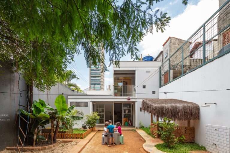 Children playing in the central courtyard of a neighborhood school with a view of the modern L-shaped extension and surrounding urban context.