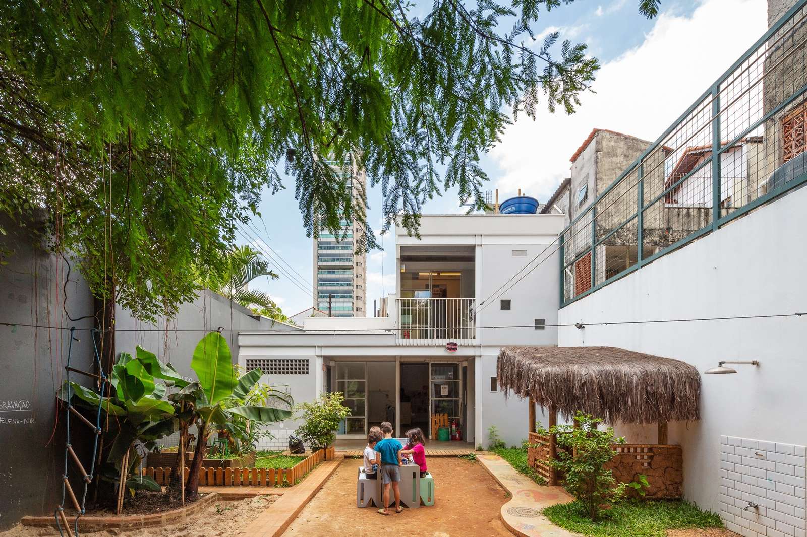 Children playing in the central courtyard of a neighborhood school with a view of the modern L-shaped extension and surrounding urban context.