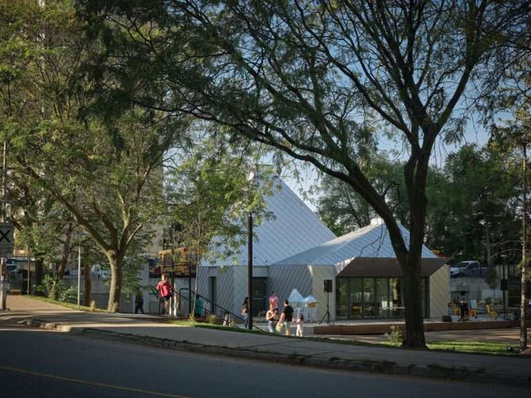 Mabelle Park public pavilion building with a metallic shingle facade viewed from across the street through mature green trees in Toronto.