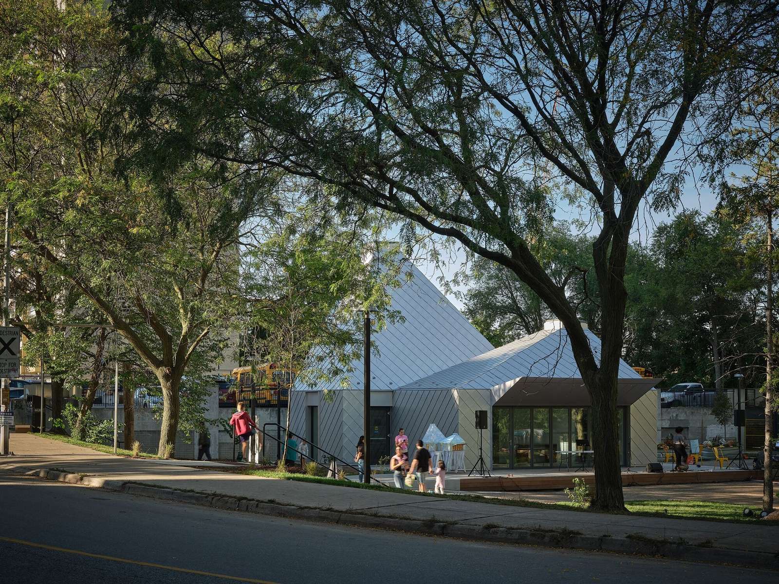 Mabelle Park public pavilion building with a metallic shingle facade viewed from across the street through mature green trees in Toronto.