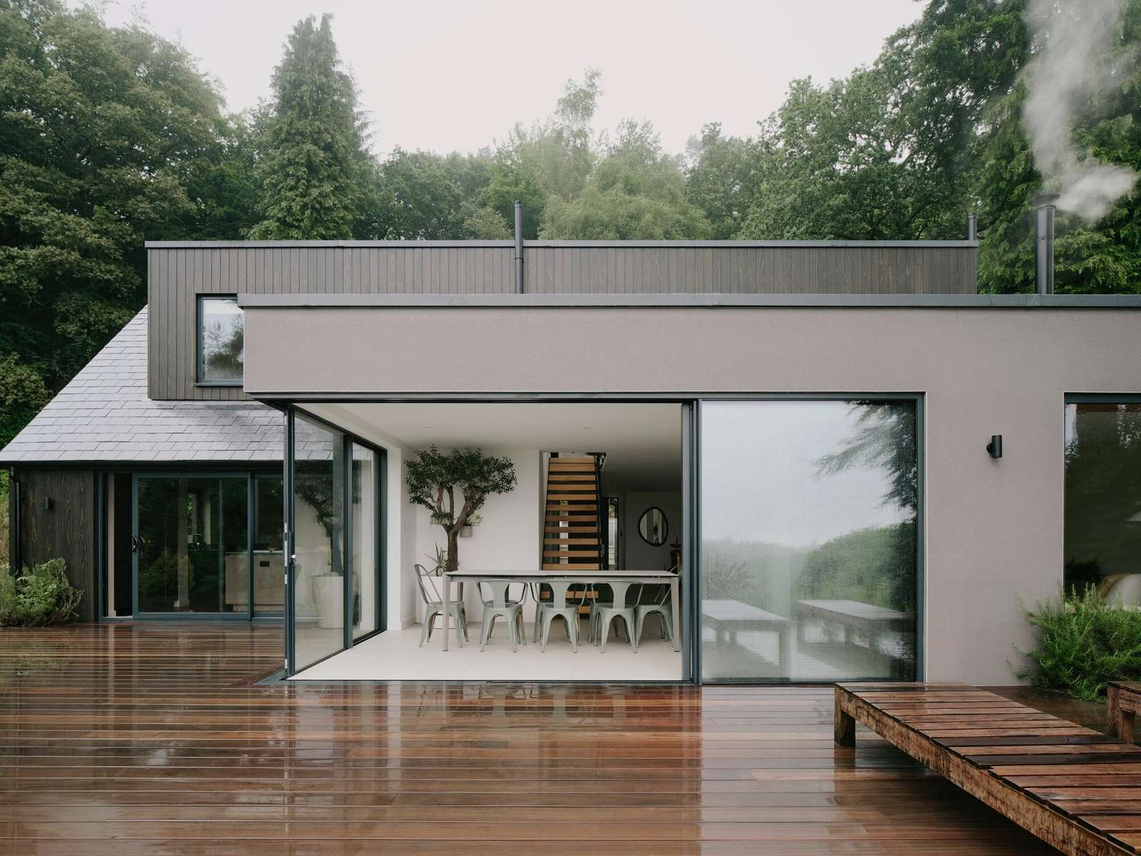 Open-plan dining area at Beech Cottage with floor-to-ceiling glass walls seamlessly connecting to a wooden deck.