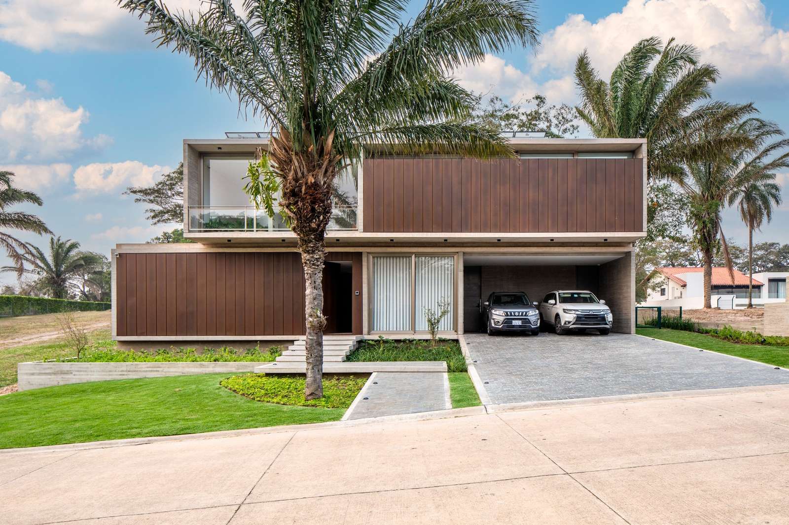 Exterior facade of Casa Jevio featuring L-shaped concrete structure, metal cladding, and integrated driveway.