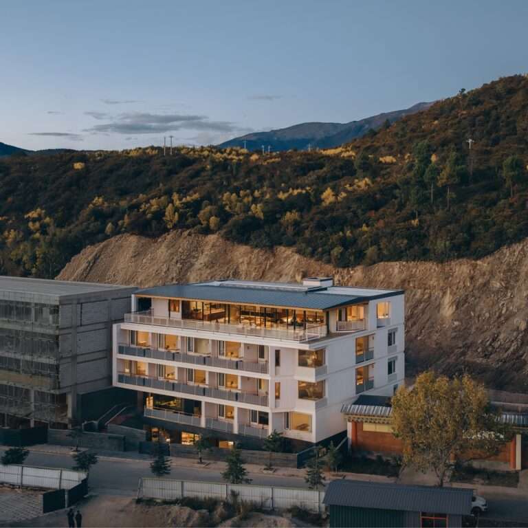 Exterior of Kawagebo Snow Mountain Hotel featuring a white sandstone facade against a mountain backdrop in Deqin Yunnan.