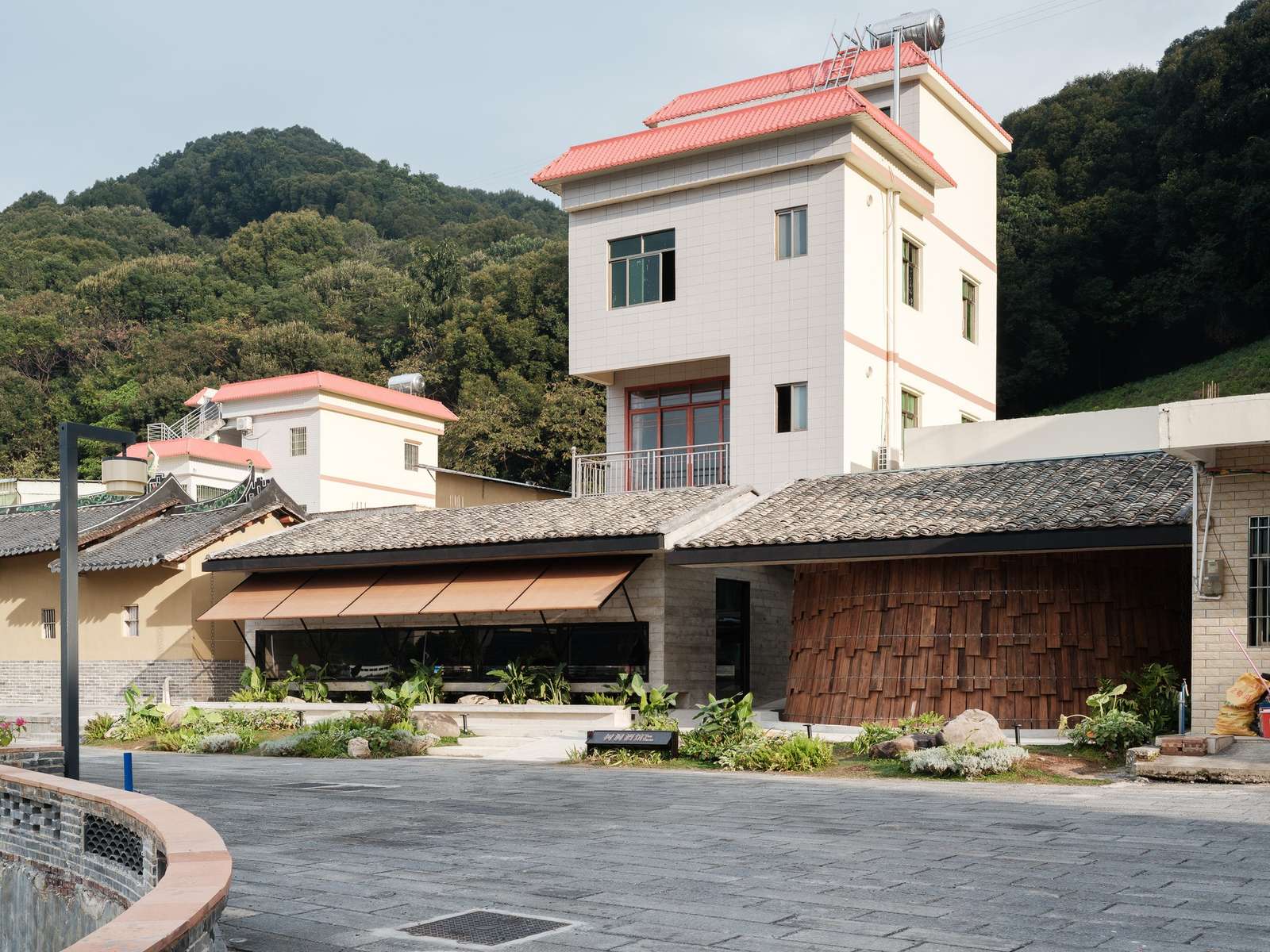 Street view of the Tree Village project featuring the modern cave teahouse with a long horizontal window and the textured wooden shingle facade of the tree tavern under traditional tiled roofs.
