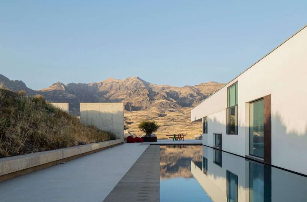 A 30-meter-long outdoor swimming pool alongside a modern white concrete villa in Rind village, reflecting the Armenian Vayots Dzor mountain landscape under a clear sky.