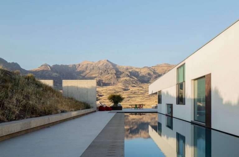 A 30-meter-long outdoor swimming pool alongside a modern white concrete villa in Rind village, reflecting the Armenian Vayots Dzor mountain landscape under a clear sky.