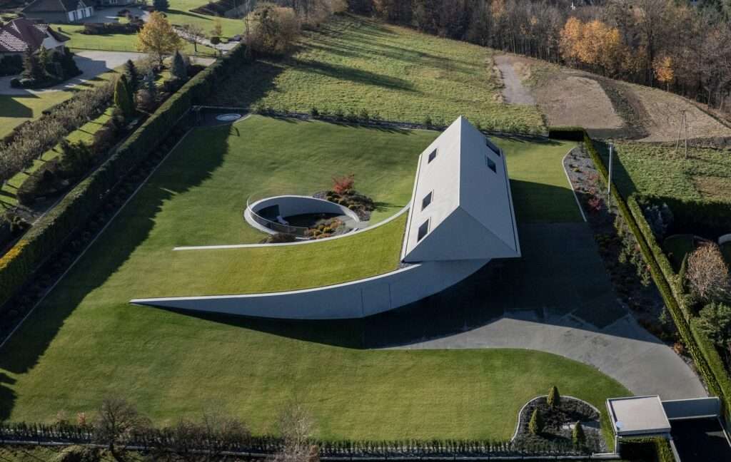 Aerial drone photograph of the Yaw House in the Beskid Mountains by KWK Promes, showing a gabled roof volume twisted on a sloping green meadow with a semi-circular courtyard.