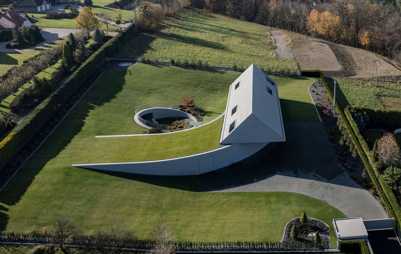 Aerial drone photograph of the Yaw House in the Beskid Mountains by KWK Promes, showing a gabled roof volume twisted on a sloping green meadow with a semi-circular courtyard.