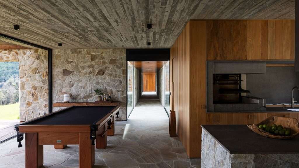 Modern interior of Casa Inter Pires featuring stone masonry walls, a billiard table, timber cabinetry, and a concrete ceiling.