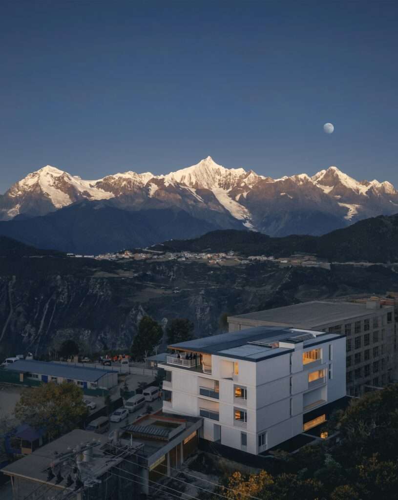 Elevated night view of Kawagebo Snow Mountain Hotel illuminated under a full moon in the Yunnan mountains.
