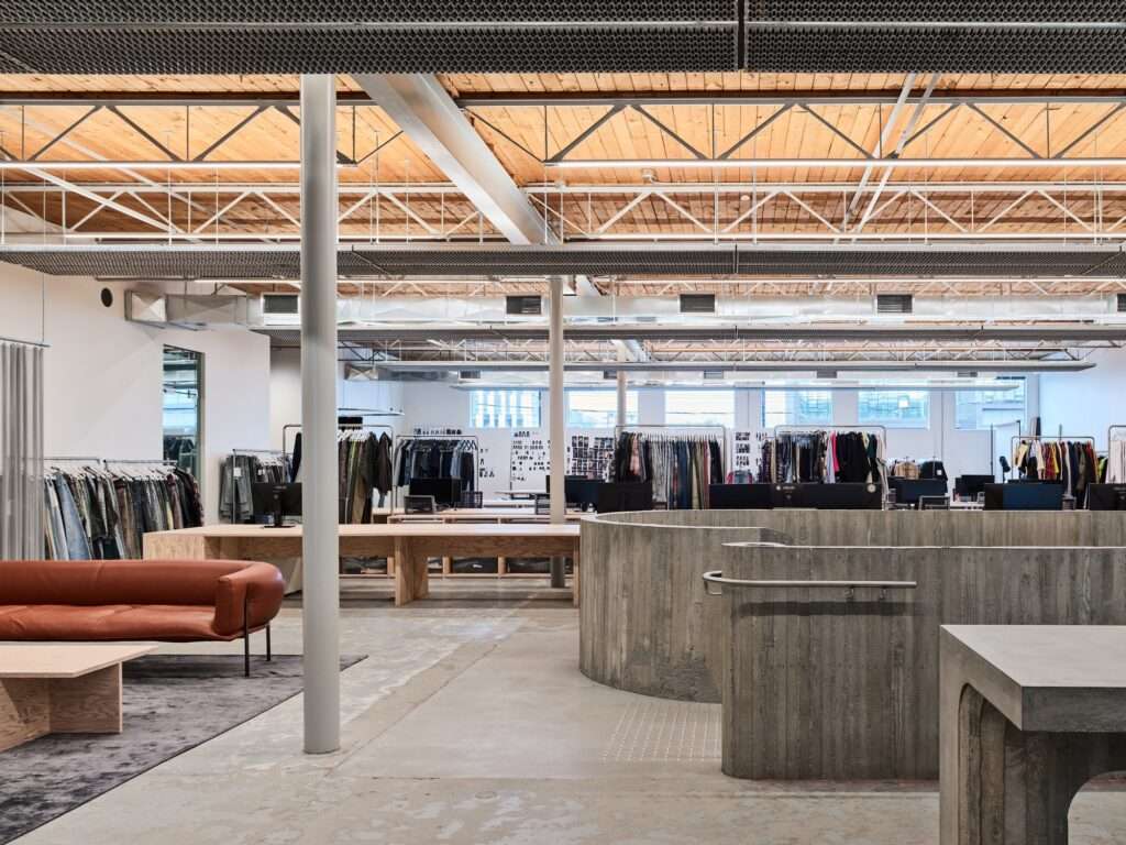 Open-plan office interior of Purple Brand Studio with exposed wooden ceilings, galvanized mesh service grids, and minimalist concrete furniture.