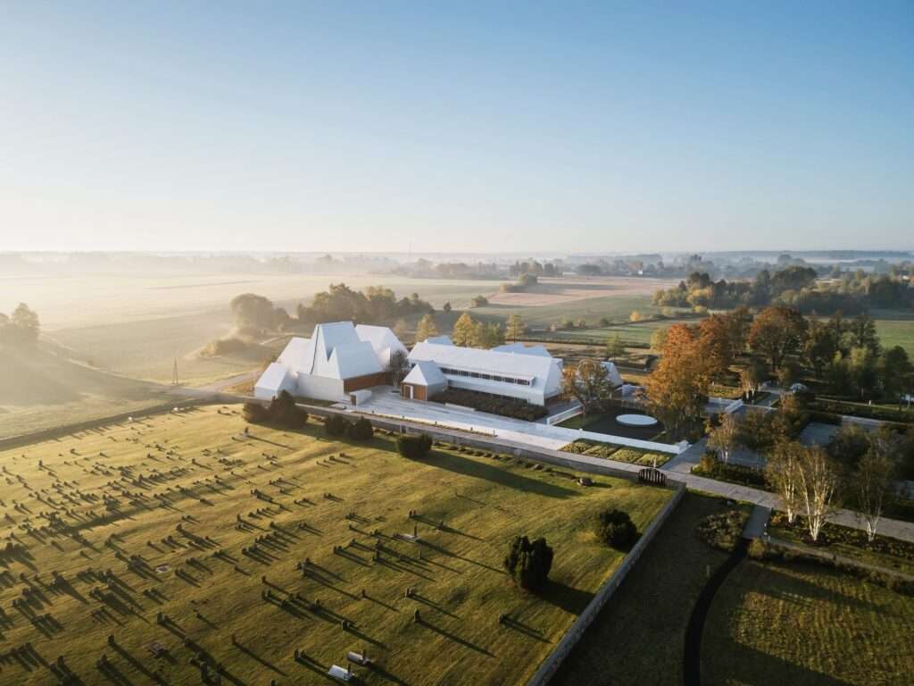 Aerial drone view of The Lost Shtetl Museum complex showing the cluster of white pitched-roof buildings and the surrounding memorial landscape in Šeduva.