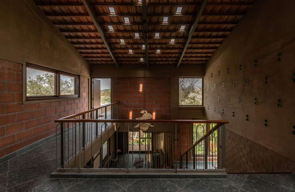 Double height interior atrium of Svatamman house with an upper level walkway, open staircase, exposed brick walls, and a structural clay filler slab ceiling.