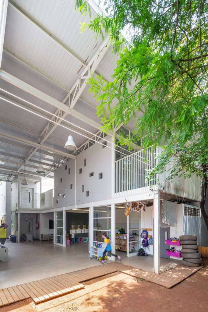 Semi-open educational spaces with high steel roofing and direct access to the outdoor dirt playground.