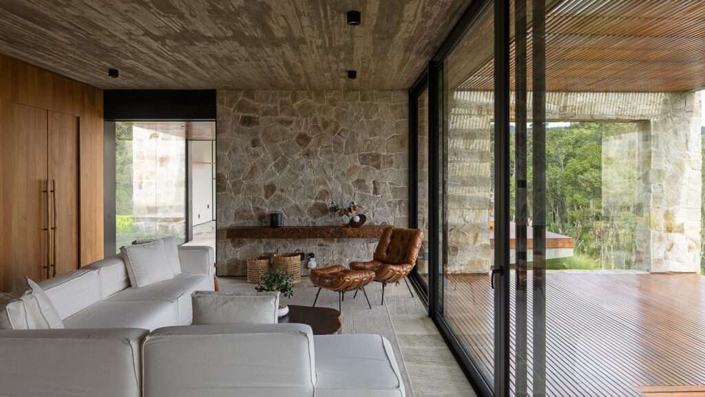 Minimalist living room with white sofa and leather armchair opening up to a wooden veranda through large glass sliding doors.