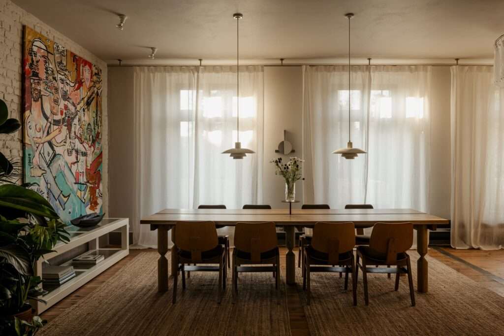 Open plan interior of P81 House with original wooden floors, a large black leather sofa, and a steel beam replacing a central wall.