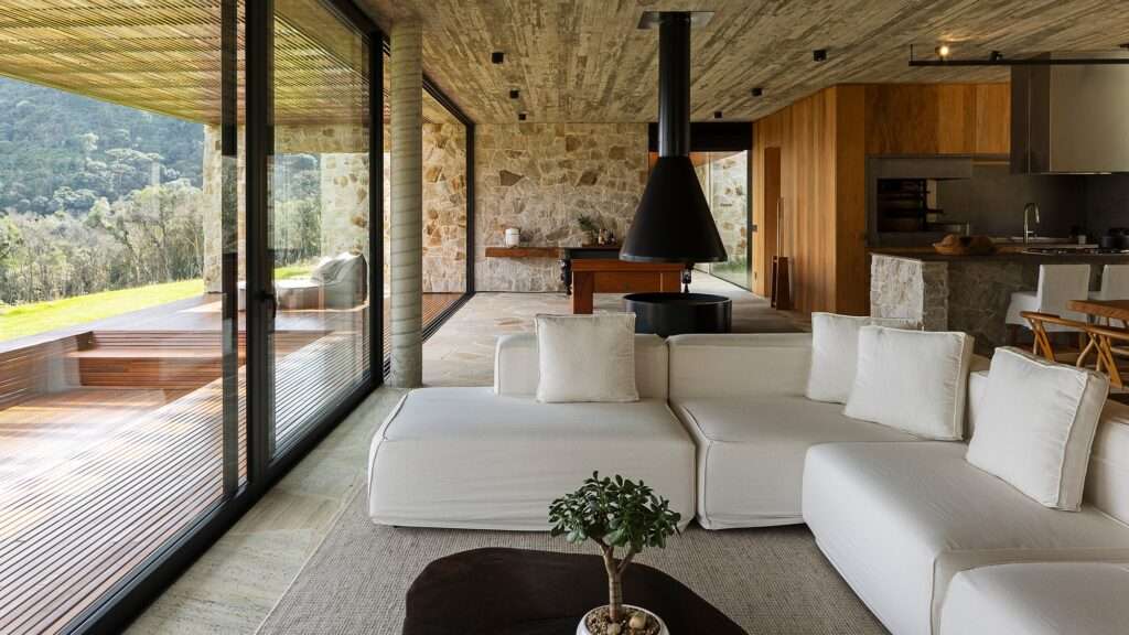 Open-plan living space in Casa Inter Pires with a white sectional sofa, suspended black fireplace, and wide outdoor timber deck.