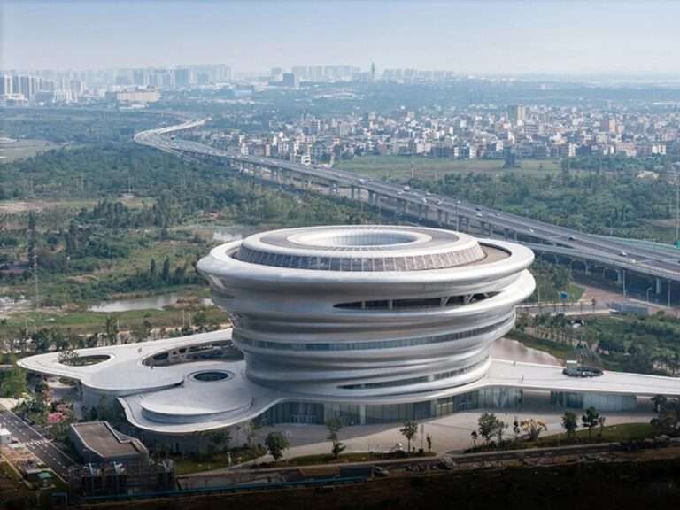 Aerial view of Hainan Science and Technology Museum by MAD Architects showing its silver spiral cloud-like structure situated next to Haikou city landscape.