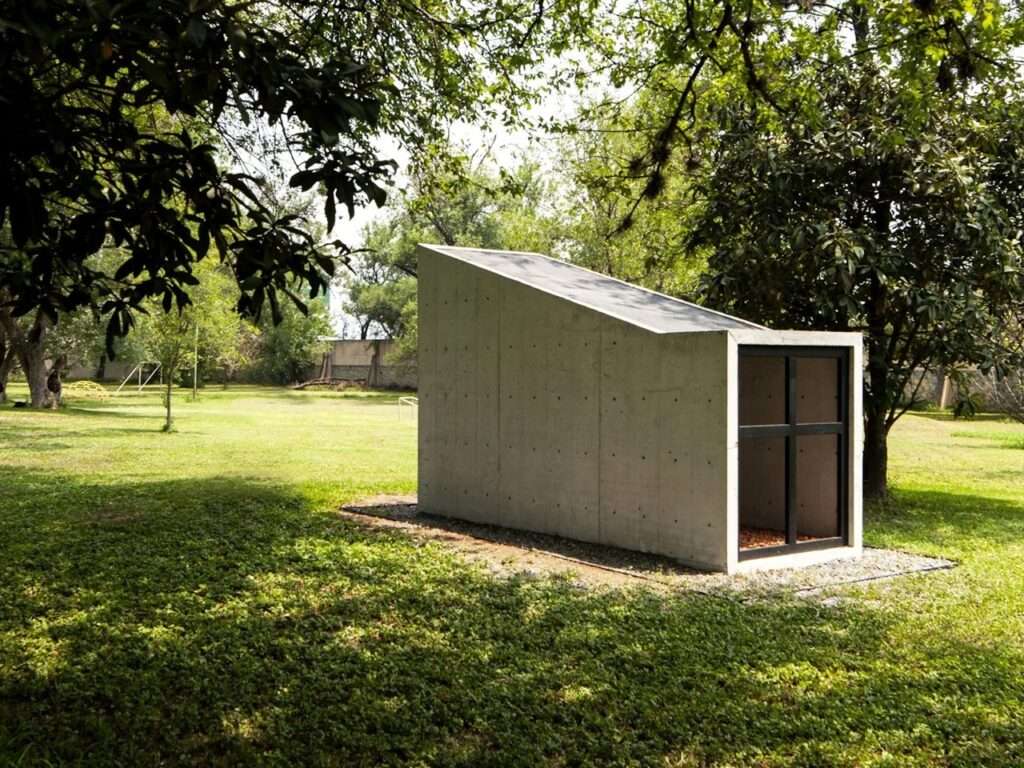 Exterior wide shot of the Oratory Chapel by S-AR in Santiago, Mexico, featuring a minimalist concrete structure integrated into a lush green garden.