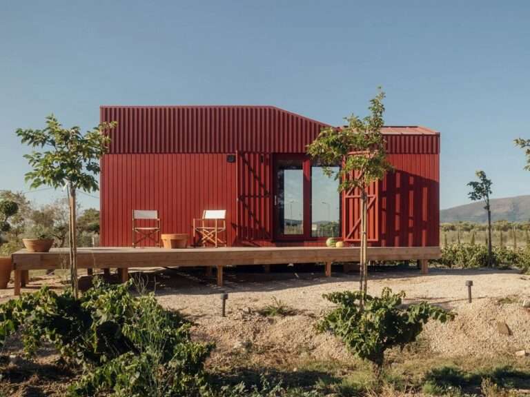 Exterior front view of Root Cabin by Kasawoo, a modular prefab red wooden cabin with a large timber deck situated in a rural vineyard landscape in Zakynthos.