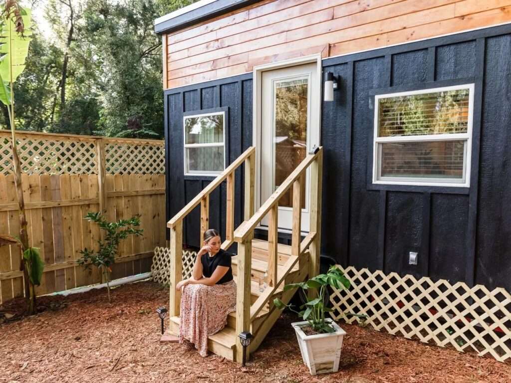 Exterior view of the 20-foot Tulsi tiny home on wheels by Simplify Further, featuring black board and batten siding combined with warm natural wood cladding on top.