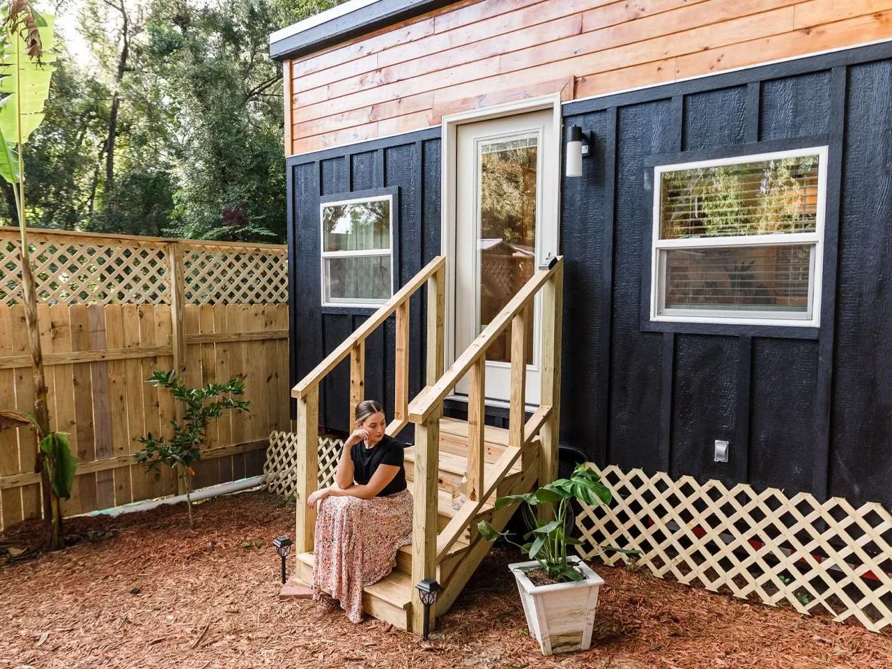 Exterior view of the 20-foot Tulsi tiny home on wheels by Simplify Further, featuring black board and batten siding combined with warm natural wood cladding on top.