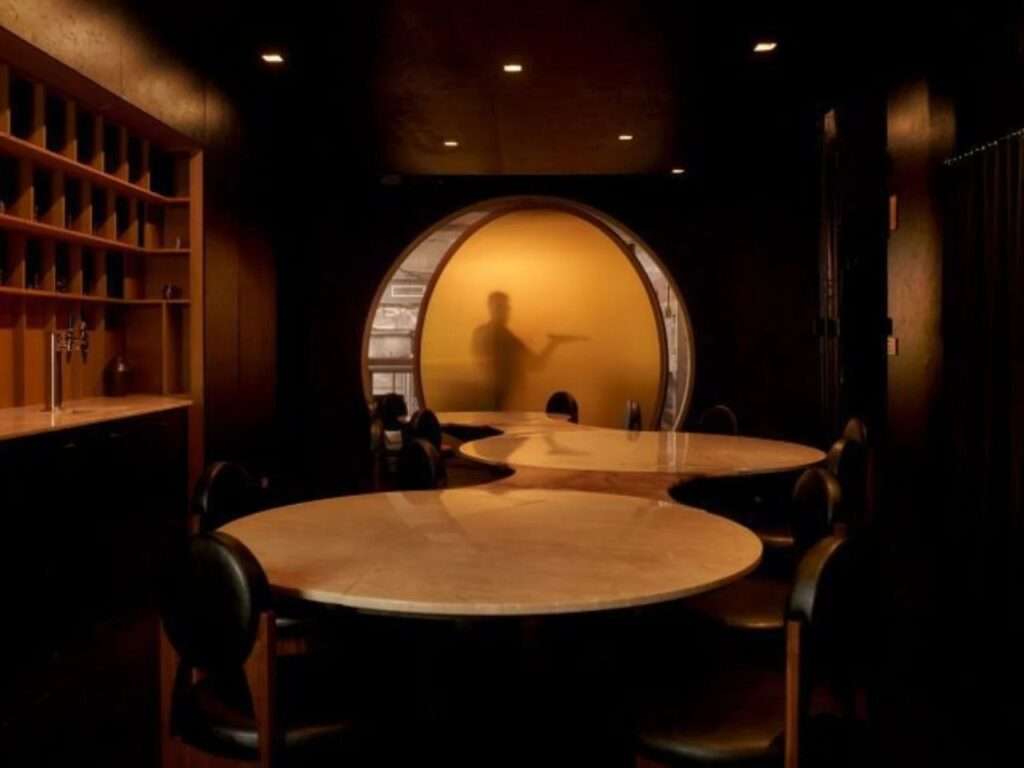 Interior view of Gourmega restaurant in Manhattan featuring a large circular alabaster communal table and a glowing yellow semi-transparent pivoting door.