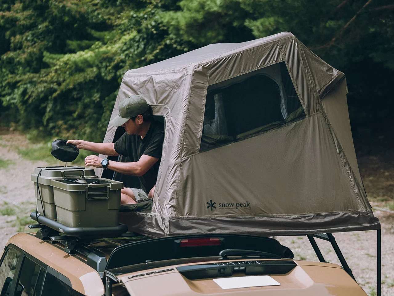A man organizing camping gear inside the Fire Rise RTT roof tent while seated at the wide side entrance.