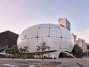 Daytime exterior view of the Seoul Robot and AI Museum (RAIM) featuring its spherical parametric envelope covered with grid-aligned curved metallic panels under a clear sky.