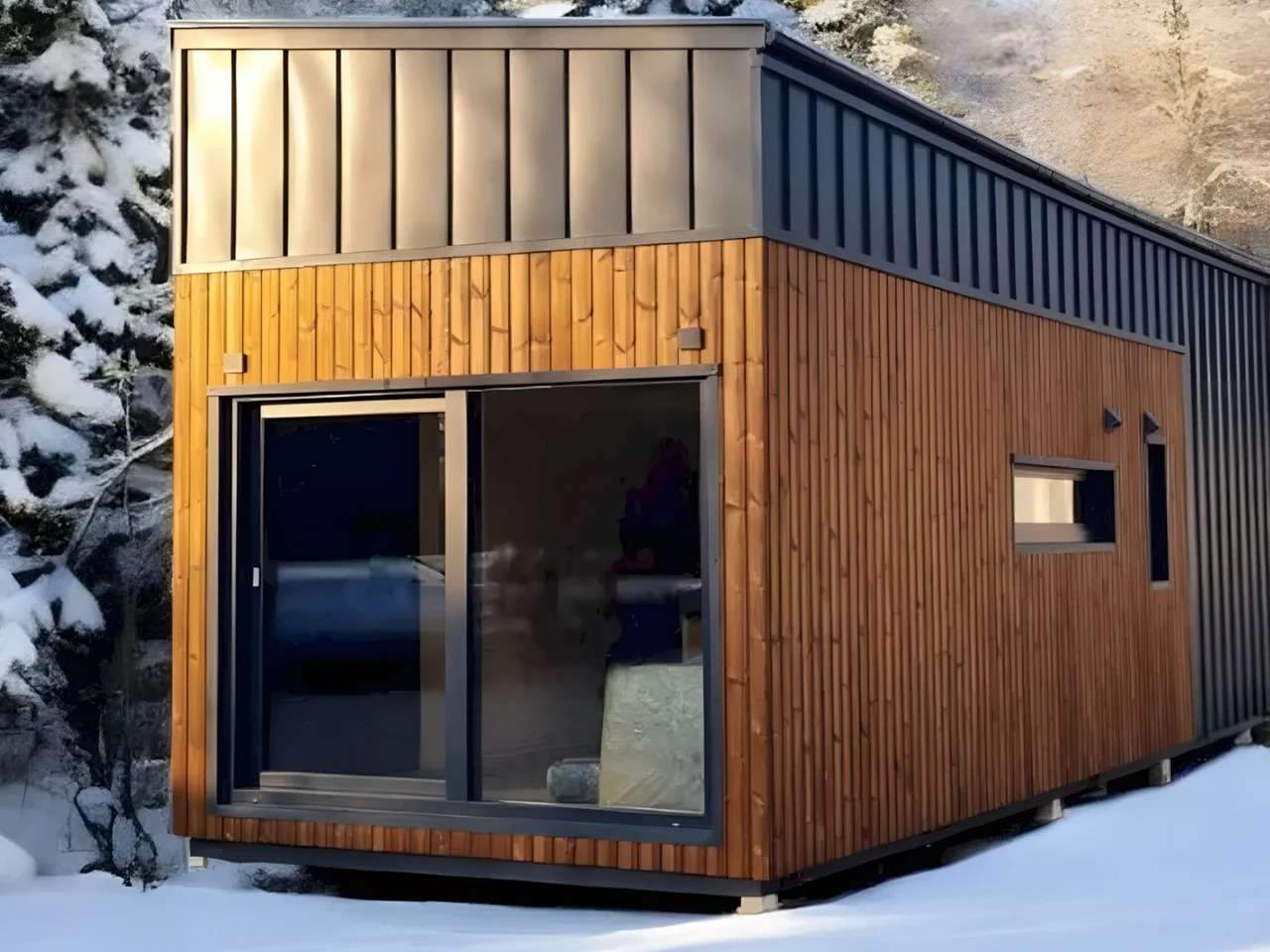 Exterior front view of the Samuel tiny house showing natural wood cladding and dark metal roofing in a snowy environment.